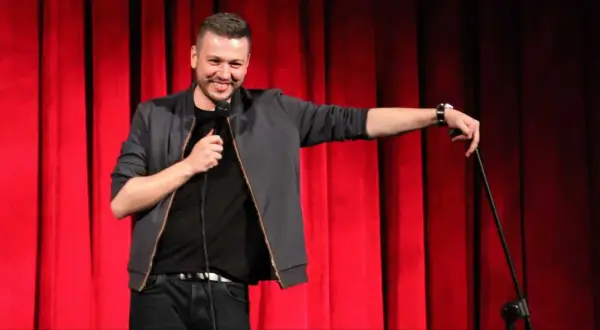 Mateusz Socha na scenie z mikrofonem, na tle czerwonej kurtyny.