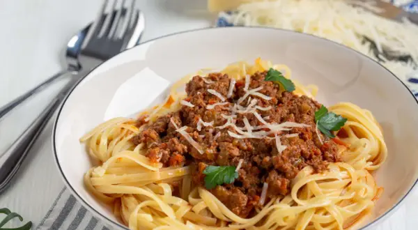 Teller mit Spaghetti Bolognese, garniert mit Parmesan und Petersilie. Ja, man kann gekochte Spaghetti Bolognese einfrieren.