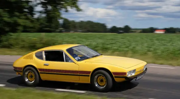 Gul vw sp2 susar fram längs en landsväg, med gröna fält och moln som suddas ut i bakgrunden.