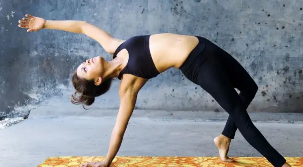 Donna in posizioni di yin yoga, con un braccio teso e il corpo arcuato all'indietro, su un tappetino colorato.