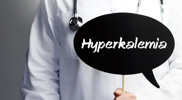 Lekarz w białym fartuchu ze stetoskopem trzyma czarną chmurkę z napisem "Hyperkalemia". Oznacza to podwyższony potas we krwi.