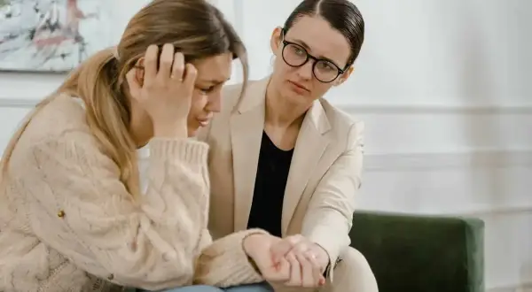 Kobieta w beżowym żakiecie pociesza smutną koleżankę. Czasem nawet urlop siła wyższa nie pomaga, gdy potrzebujemy wsparcia.