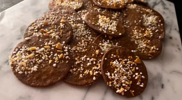 En hög med runda, mörka kakor med mandelmjöl och choklad, toppade med hackade nötter och pärlsocker. Perfekta till fikat!
