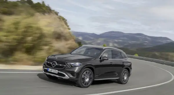 Czarny Mercedes GLC 200 4MATIC pokonuje zakręt na górskiej drodze, otoczony zielonymi wzgórzami i skalistymi zboczami.