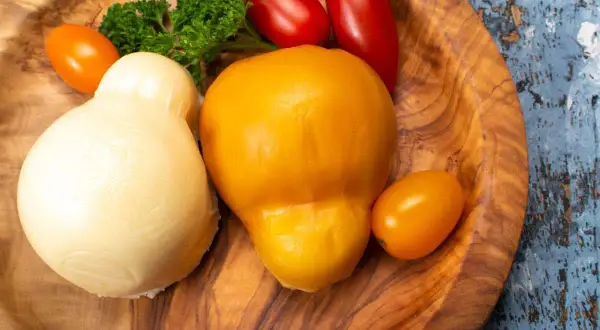 Due forme di formaggio, una bianca e una gialla, che sembrano provola e scamorza, sono la stessa cosa. Accanto, pomodorini e prezzemolo.