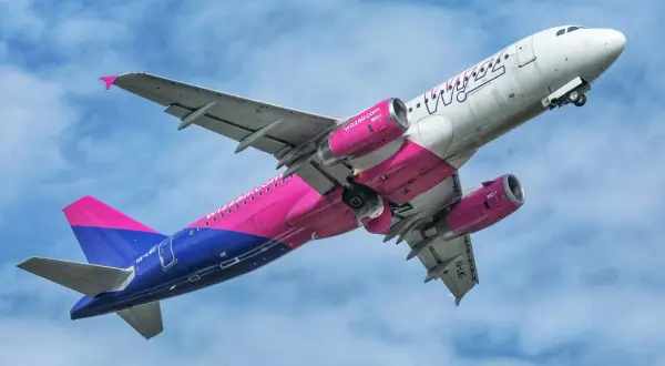 Samolot Wizzair z różowo-niebieskim malowaniem wznosi się na tle błękitnego nieba. Może to być symbol nadziei na nowy, odwołany lot Wizzair.
