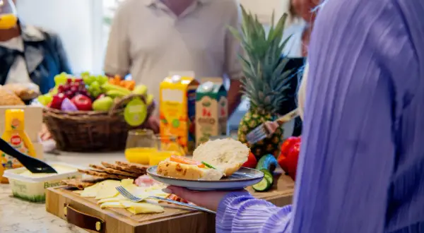 En härlig frukost på jobbet med frukt, ost, kex och färska bullar. En person tar en smörgås.
