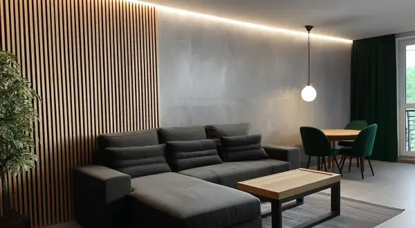 Nowoczesny **styl industrialny salon loft** z szarą sofą, drewnianą ścianą i zielonymi akcentami.