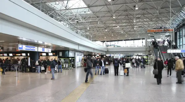 Tłoczny terminal lotniska Rome Ciampino, ludzie z bagażami czekają w kolejce do odprawy.