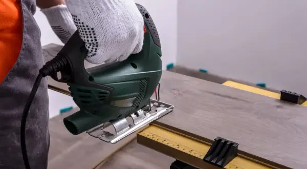 Mit einem Stichsäge wird Laminat schneiden. Ein Handwerker mit Handschuhen arbeitet präzise.