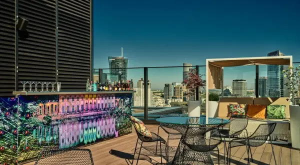 Elegancki ether rooftop bar z widokiem na miasto. Kolorowy bar, stoliki i wygodne fotele zapraszają do relaksu.