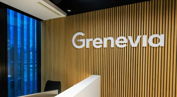 Nowoczesne biuro z logo Grenevia na drewnianej ścianie. Za oknem błękitny, deszczowy krajobraz miejski.