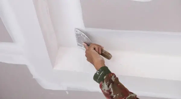 Mano aplicando masilla para techo escayola con espátula, alisando juntas y esquinas para un acabado perfecto.