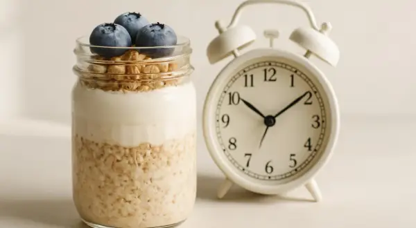 Barattolo con yogurt, mirtilli e fiocchi d'avena, accanto a una sveglia. La colazione è pronta!