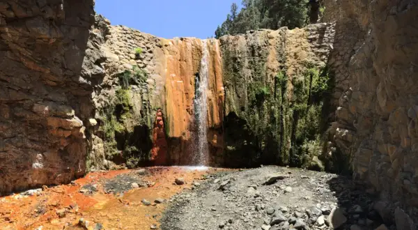 Cascada rojiza y verde en un cañón rocoso, ideal para senderismo en Palma de Mallorca.