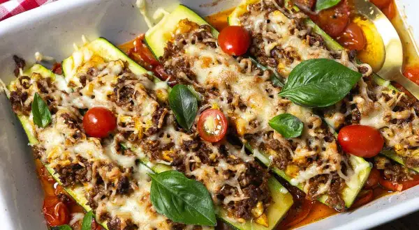 Herzhafte zucchini schiffchen mit Hackfleisch und Käse überbacken, garniert mit frischem Basilikum und Kirschtomaten.