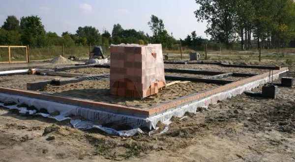 Stan zero budynku w budowie. Fundamenty z cegły i folii, stosy pustaków.