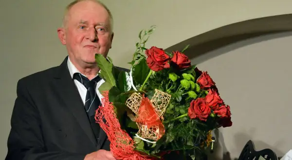Starszy mężczyzna w garniturze trzyma bukiet czerwonych róż i zielonych kwiatów.