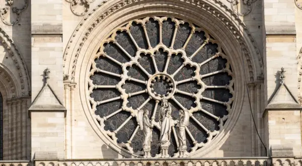 Ein Rosettenfenster im Stil der Gotik-Kunst, umrahmt von Steinfiguren und filigranen Verzierungen an einer Kathedrale.