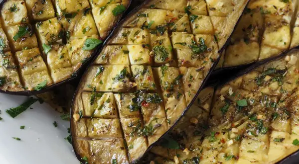 Gegrillte Auberginenhälften, mit Kräutern und Knoblauch gewürzt, bereit zum Servieren. Ein köstliches Gericht, das die Aromen des Ofens einfängt.