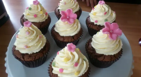 Sju chokladmuffins med fluffig vit choklad frosting, dekorerade med rosa blommor och strössel. Perfekt för ett kalas!