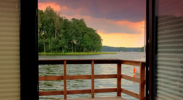 Drewniany pomost z widokiem na jezioro i las o zachodzie słońca.