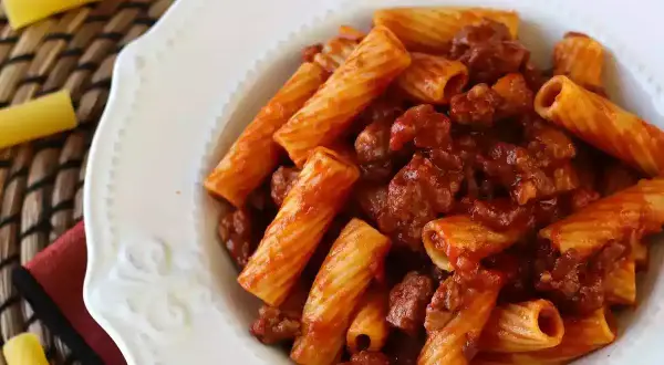 Piatto di pasta con salsiccia e sugo rosso, servita in un piatto bianco decorato.