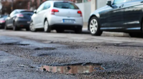 Poprzeczna nierówność jezdni z kałużami i zaparkowanymi samochodami.