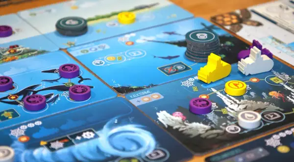 Ein komplexes Brettspiel mit Meeresmotiven. Lila und gelbe Spielsteine auf blauen Karten mit Walen und Quallen. Ein Kennerspiel, das strategisches Denken erfordert.