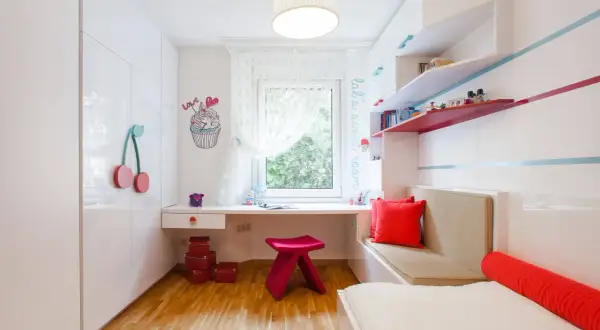 Ein heller Schreibtisch vor dem Fenster in einem Kinderzimmer, mit bunten Akzenten und Spielzeug.