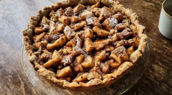 Apetyczna tarta na słodko z jabłkami i kruszonką, posypana cukrem pudrem. Idealna na deser.