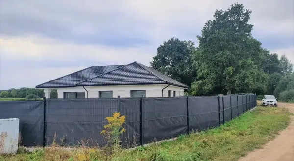 Nowoczesna siatka ogrodzeniowa skutecznie zasłania płot, zapewniając prywatność. Dom i samochód w tle.