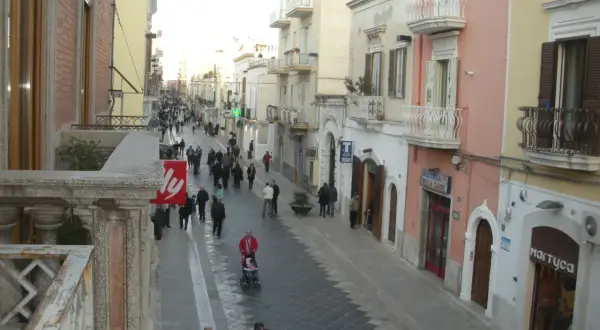 Passeggiata serale per gli abitanti di Manfredonia in una via commerciale animata, con negozi e palazzi storici.