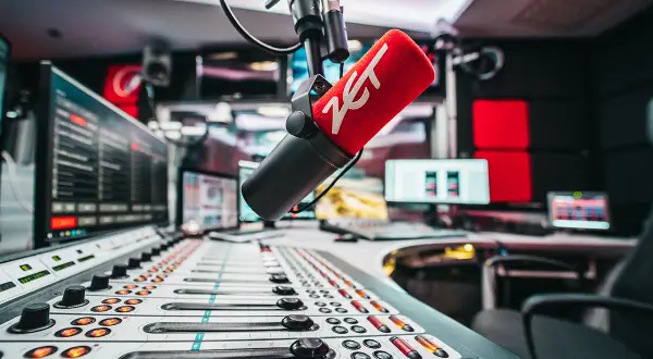 Mikrofon radiowy z logo ZET na tle konsolety i monitorów w studiu.