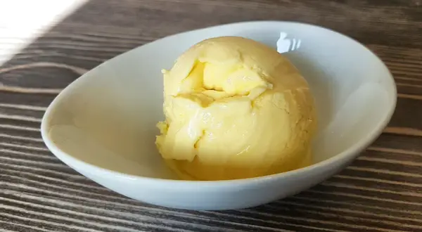 Cremiges Mango-Eis, selbst gemacht mit der Eismaschine, in einer weißen Schale auf Holztisch.