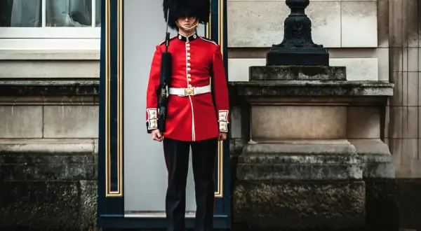 Un guardia con uniforme rojo y sombrero de piel, un típico inglés, vigila la entrada de un edificio histórico.