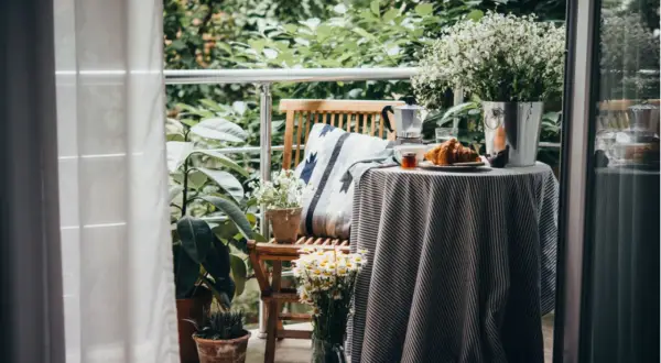 Gemütlich einen kleinen Balkon gestalten: Frühstück mit Kaffee, Croissant und Blumen auf dem Tisch.
