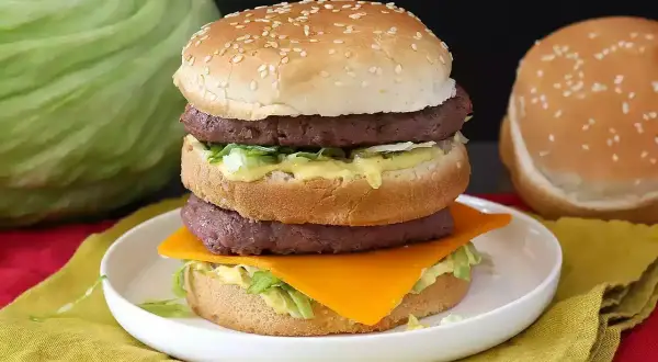 Domowy Big Mac z dwoma kotletami, serem, sałatą i sosem na talerzu.