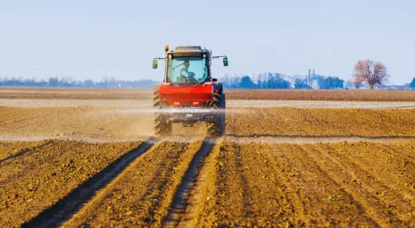 Czerwony traktor rozsiewa wapno z magnezem na polu, przygotowując ziemię do nowego sezonu.