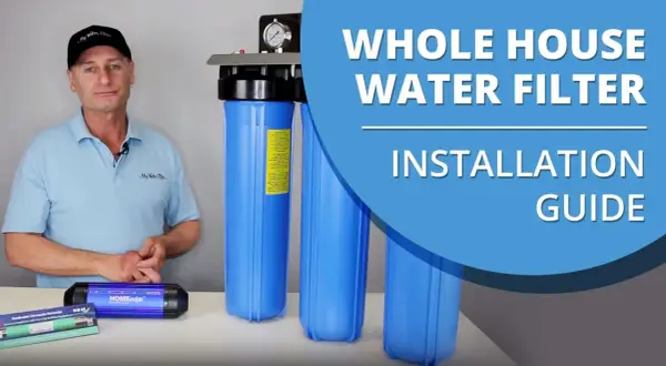 Man in a cap and polo shirt stands next to a whole house water filter system, ready for installation.