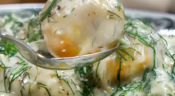 En sked lyfter upp en bit krämig dillstuvad potatis, täckt av färsk dill och en len sås.