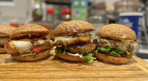 Trois burgers gras appétissants, garnis de fromage fondant, légumes frais et tomates séchées, prêts à être dégustés.