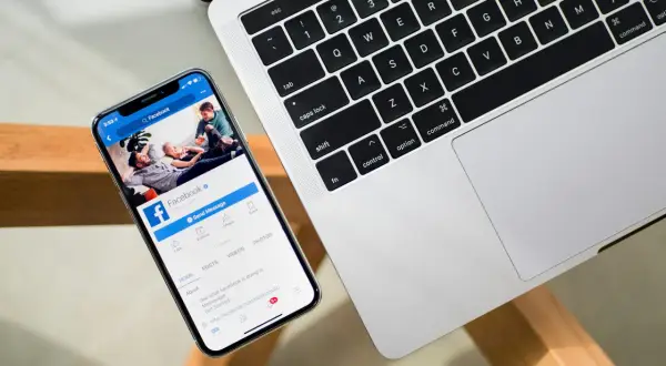 Chcesz wiedzieć, jak sprawdzić na jakich urządzeniach jesteś zalogowany na FB? Na ekranie telefonu widać stronę Facebooka, obok klawiatura laptopa.