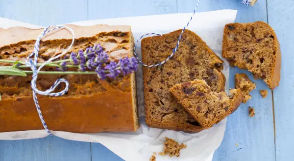 Pokrojony chlebek bananowy z gałązką lawendy i sznurkiem na niebieskim tle.