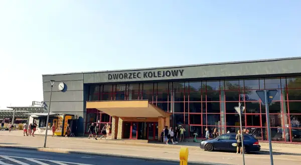Dworzec kolejowy w Krakowie, z ludźmi i samochodami przed wejściem.