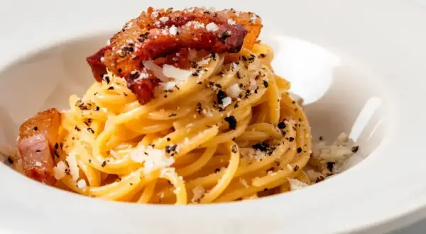 Pyszne spaghetti all'amatriciana z chrupiącym guanciale i startym parmezanem, posypane świeżo mielonym pieprzem.