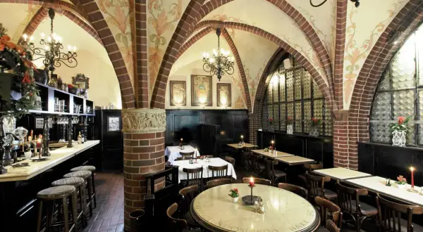 Gemütliche Atmosphäre in einem Berliner Restaurant mit Gewölbedecke, Kronleuchtern und Holztischen.
