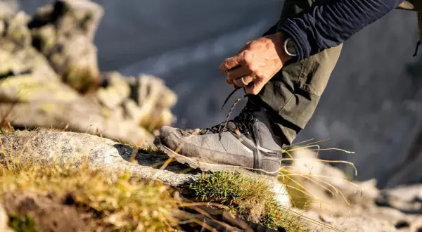 Mężczyzna sznuruje buty trekkingowe na kamieniu. Czy buty trekkingowe powinny być większe? Odpowiedź tkwi w komforcie i ochronie palców.