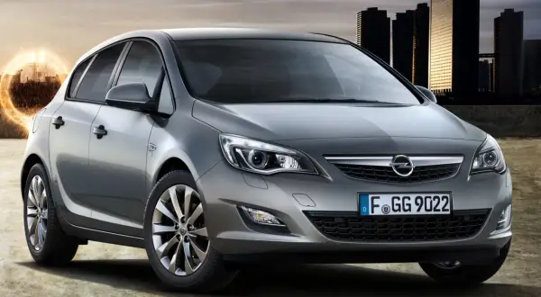 Szary Opel Astra J 1.4 Turbo 140 KM na tle miasta. Opinie o tym modelu są pozytywne.