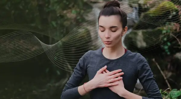 Kobieta z zamkniętymi oczami praktykuje techniki oddychania pranayama na tle natury.